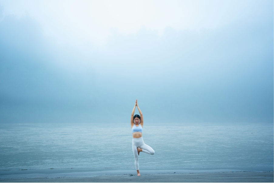 A woman practicing yoga on the beach with a view of the sea and sky in the background